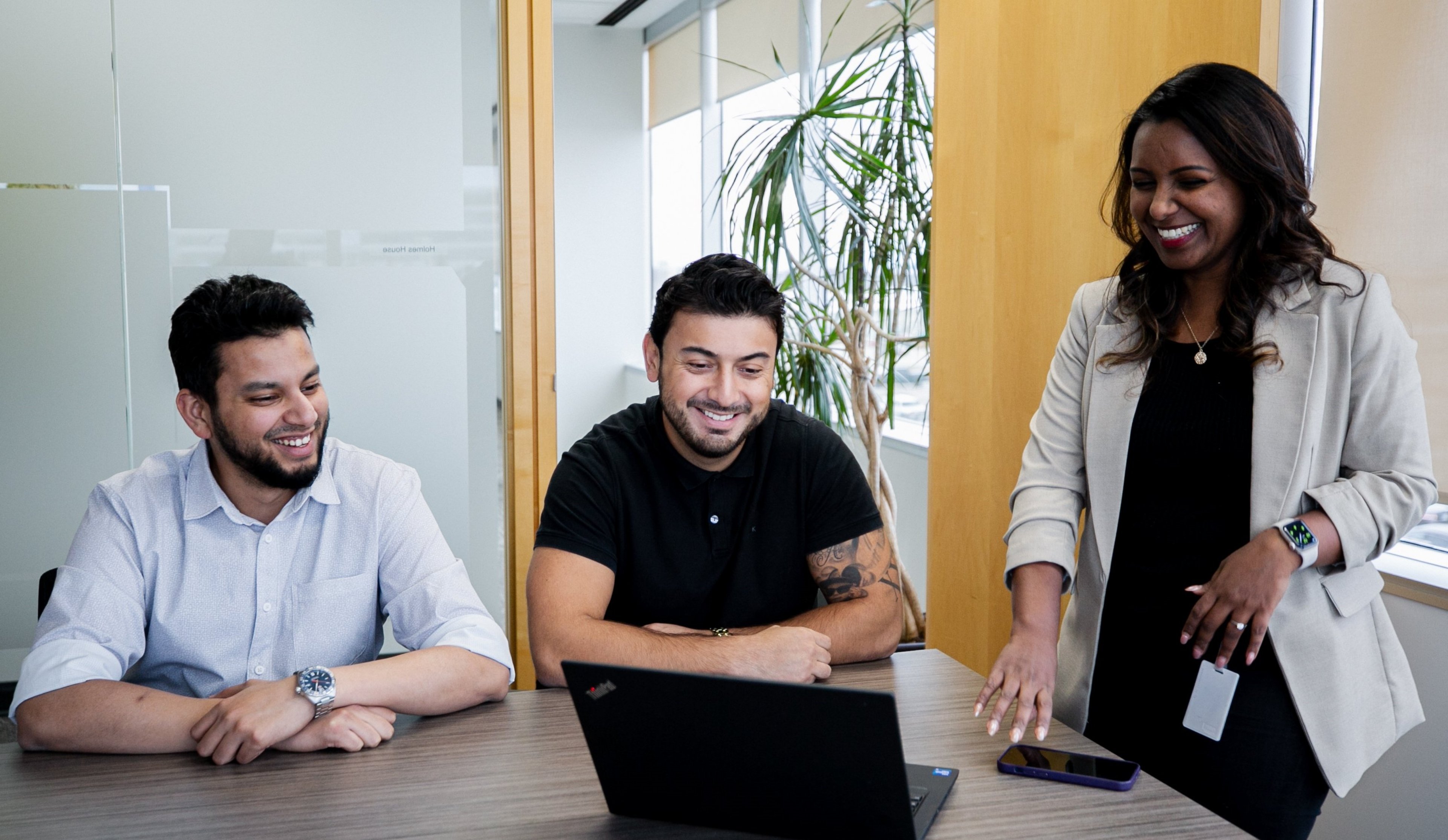 Three people in the office smiling in front of a laptop