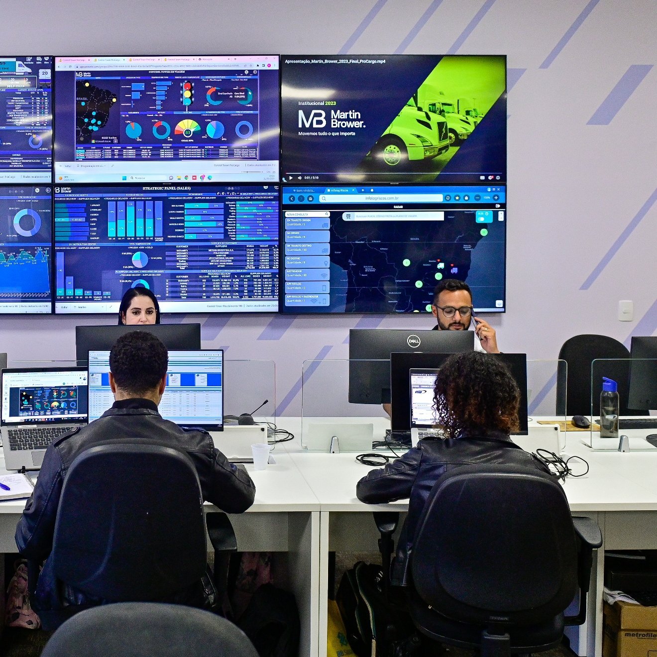 Four people working at desks with several monitors posted on the walls displaying metrics