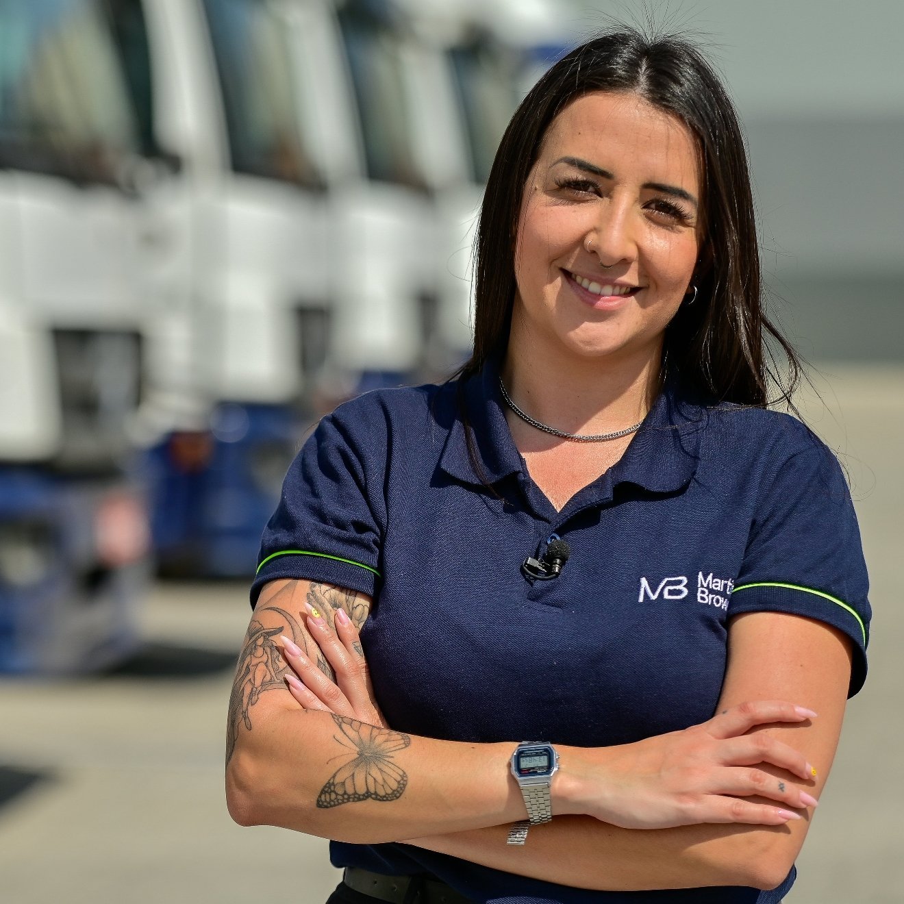 Woman wearing polo shirt with her arms crossed in front of trucks