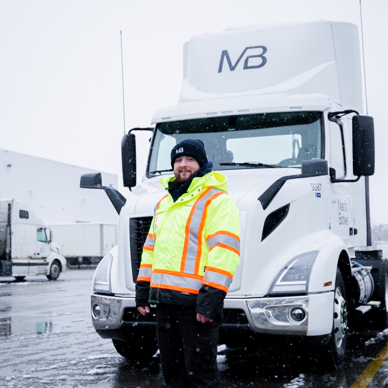 Man in a winter clothes standing in front of a truck while snow falling at the background